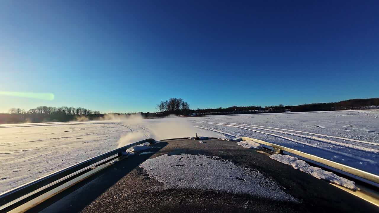 Ego-Perspektive auf ein Autodach, das sich durch Schneenebel unter blauem Himmel bewegt.