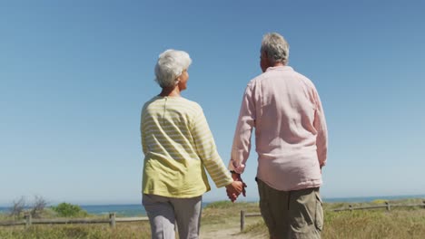 Pareja-Caucásica-Mayor-Tomándose-De-La-Mano-Y-Caminando-Por-El-Camino-Que-Conduce-A-La-Playa