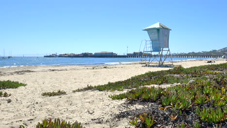 An-Einem-Sonnigen,-Klaren-Tag-In-Santa-Barbara,-Kalifornien,-Am-Sandstrand-Stehen-Und-Die-Blauen-Wellen-Am-Ufer-Mit-Einem-Leeren-Rettungsturm-Beobachten