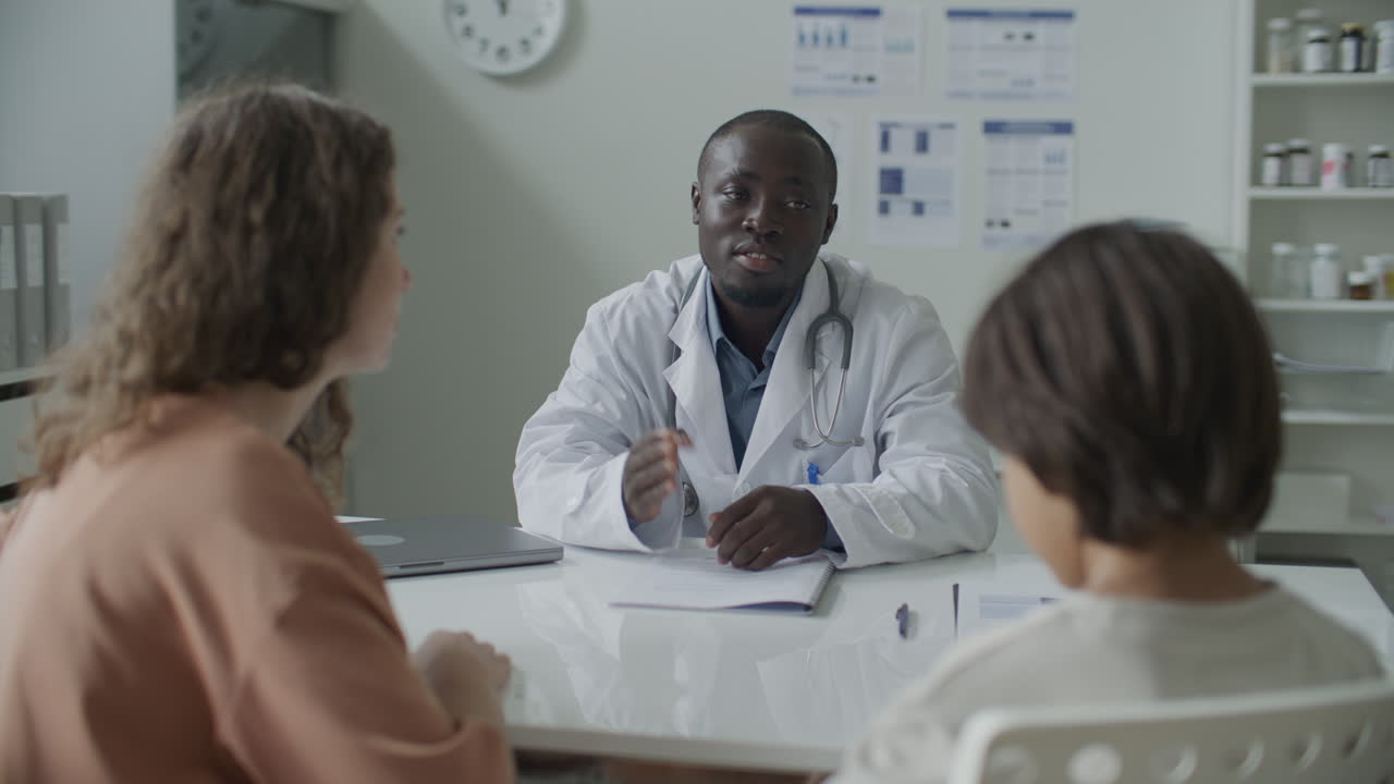 Black Pediatrician Speaking with Mother and Kid in Medical Office