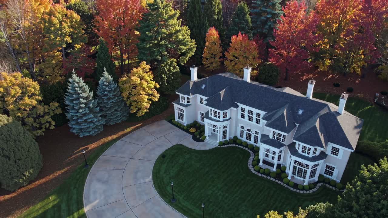 Aerial view of a large mansion surrounded by vibrant autumn trees, showcasing a luxurious lifestyle