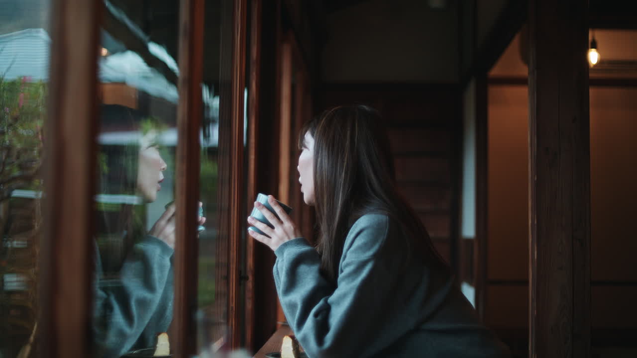 차 한 잔 을 들고 창문 밖 을 바라보는 여자