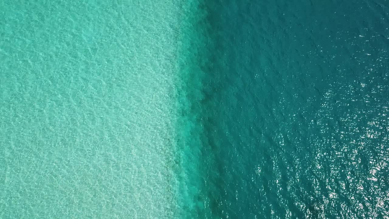 Ripresa aerea, dall'alto, con drone, sopra l'oceano turchese, color acqua marina, che si affaccia su una linea che separa l'acqua bassa della laguna dal mare più profondo color verde-blu, in una giornata di sole, alle Maldive