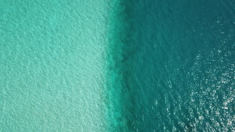 Aerial,-top-down,-drone-shot,-over-turquoise,-aqua-menthe-ocean,-overlooking-a-line-between-shallow,-lagoon-water-and-deeper-teal-colored-sea,-on-a-sunny-day,-in-Maldives