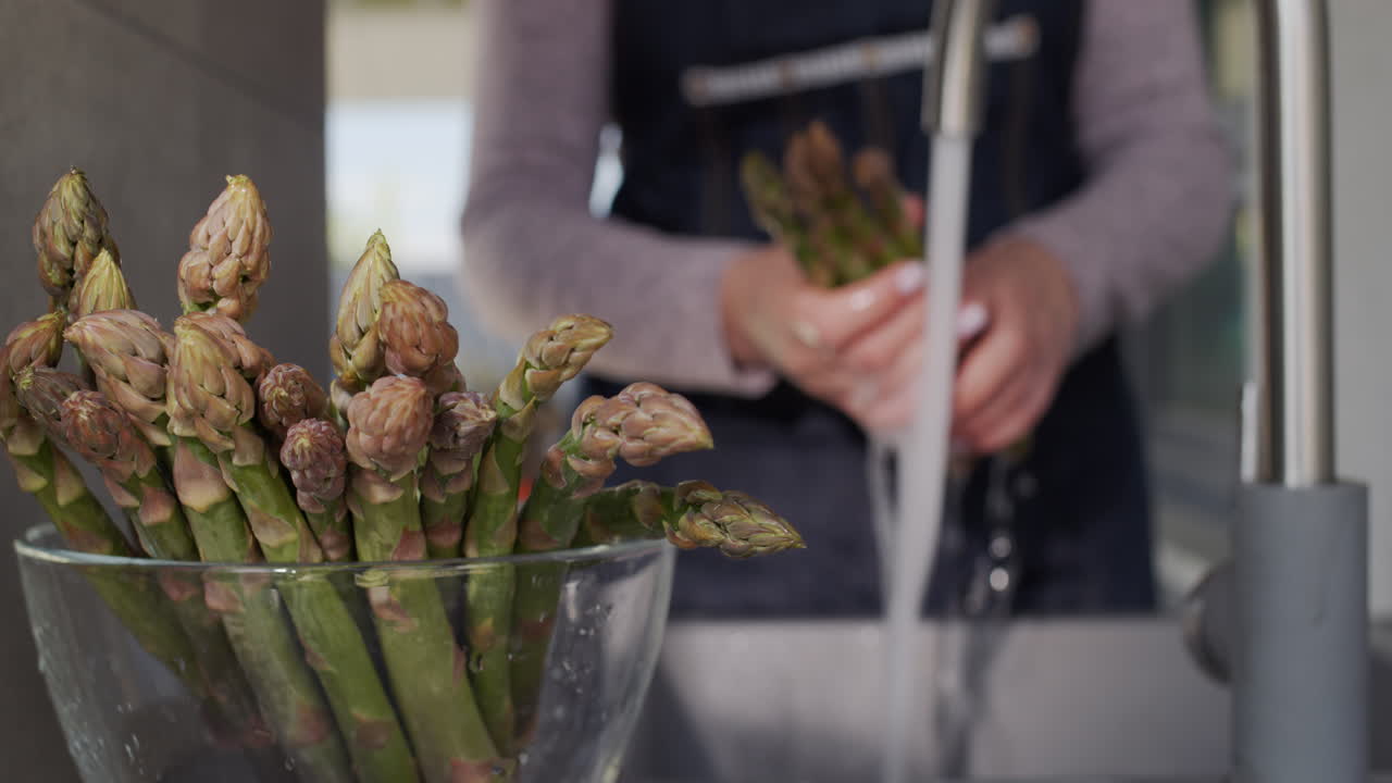 여자의 손은 수도꼭지에서 나오는 물줄기 아래에서 아스파라거스를 씻는다