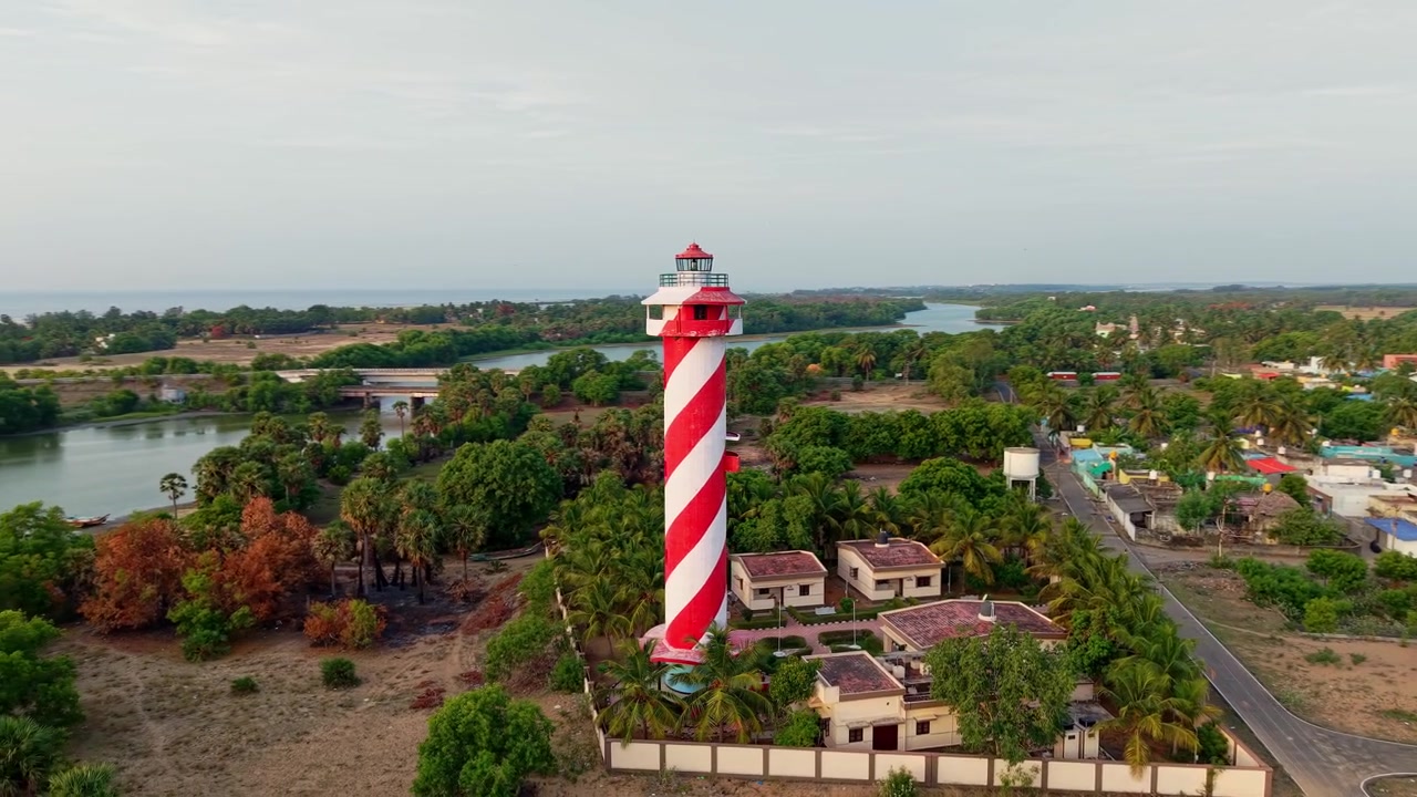 Vista aerea con drone di un faro a strisce circondato da un villaggio costiero, vegetazione lussureggiante e lagune vicino alla costa di Chennai, che mostra un paesaggio costiero suggestivo