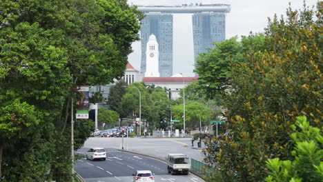 street view of pedestrians and cars driving in singapore, marina bay sands hotel in the background.