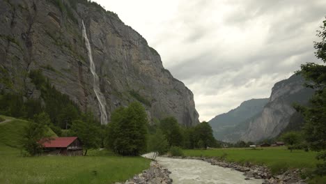 staubbach cae corriendo por un acantilado rocoso cerca del río lutschine en un prado verde y un bosque de pinos en un día nublado, lauterbrunnen, alpes suizos