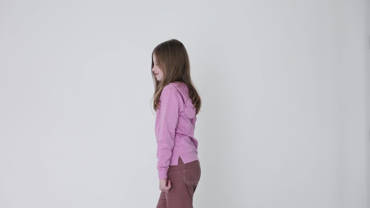 Young girl in pink hoodie turning and looking back over her shoulder against a white background