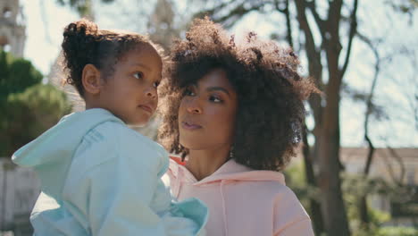 mom holding adorable daughter walking on street close up. mother carrying child.