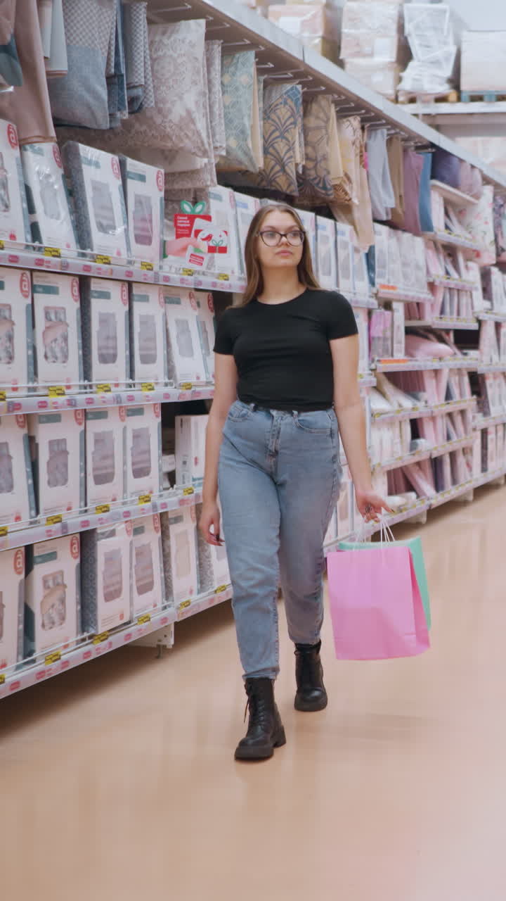 mujer caminando por el pasillo del supermercado, mirando los productos de cama en los estantes mientras otros compradores pasan, estantes de la tienda abastecidos con cubiertas de edredón y mantas de cama en el fondo