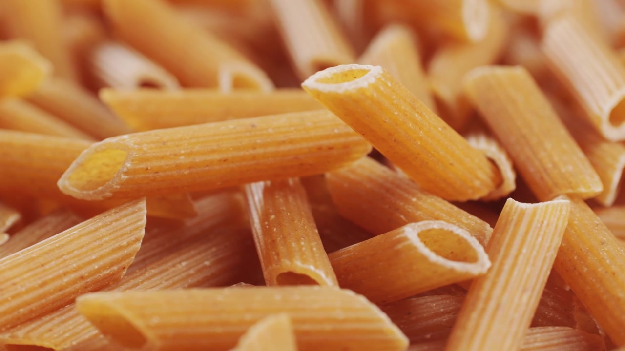 Pasta integrale biologica, maccheroni di semola di grano duro, penne rigate crude in una ciotola di legno. Filmato 4k di alta qualità