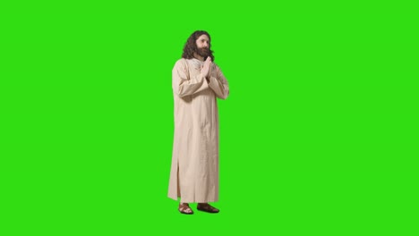 tomada de estudio de un hombre vestido con túnicas y sandalias con cabello largo y barba que representa la figura de jesucristo orando en la pantalla verde 1