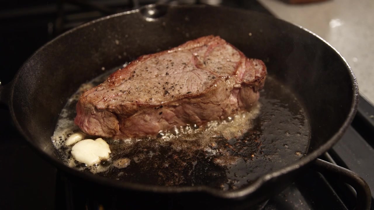 New juicy steak sizzling in butter oil with garlic. Cast iron skillet cooking beef meat