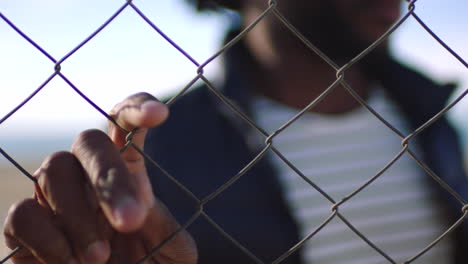 closeup of man resting hand on a chain link fence