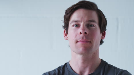 Portrait-Of-Serious-Man-Wearing-T-Shirt-Standing-Against-White-Studio-Wall