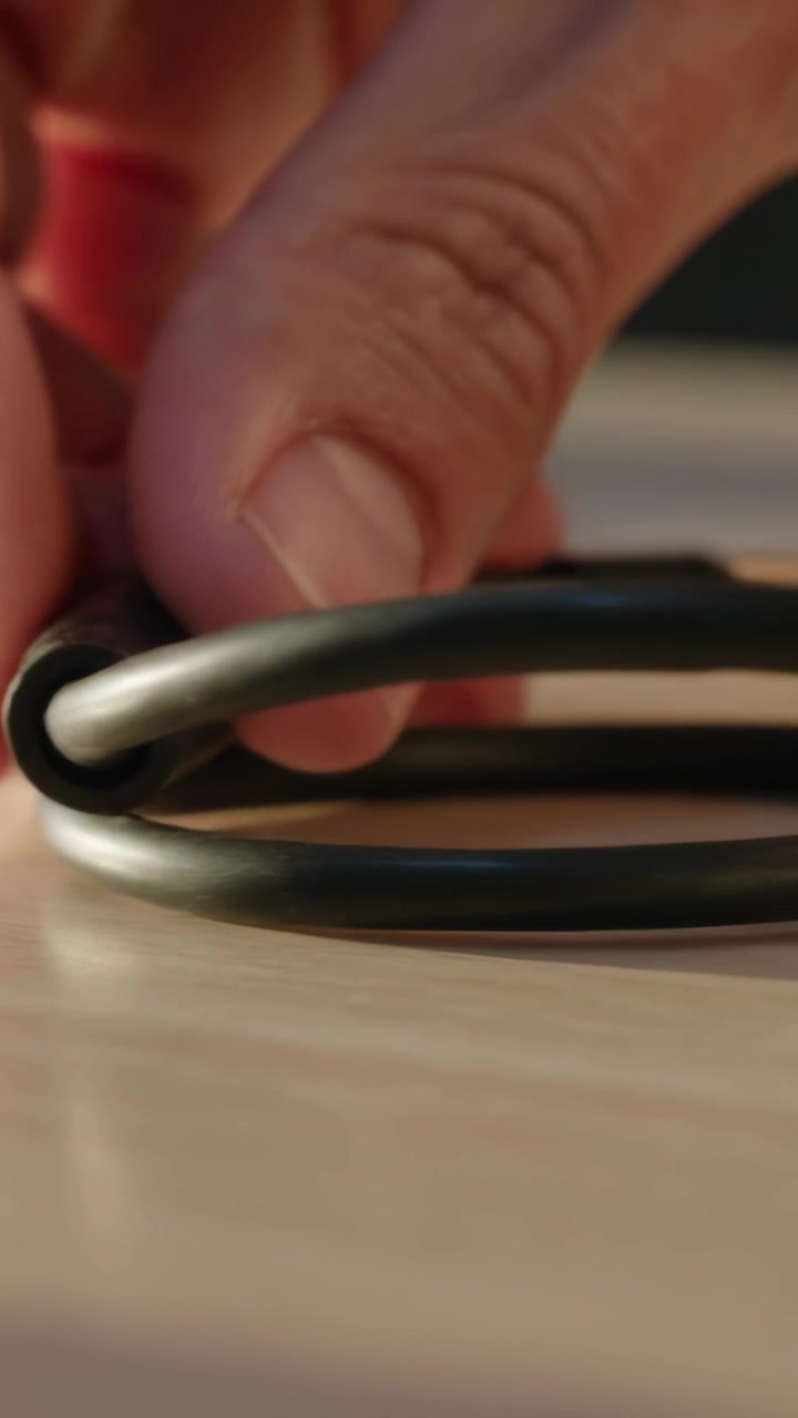 Vertical video: Approaching hand pinching and coiling black cable on desk forming coil with plug