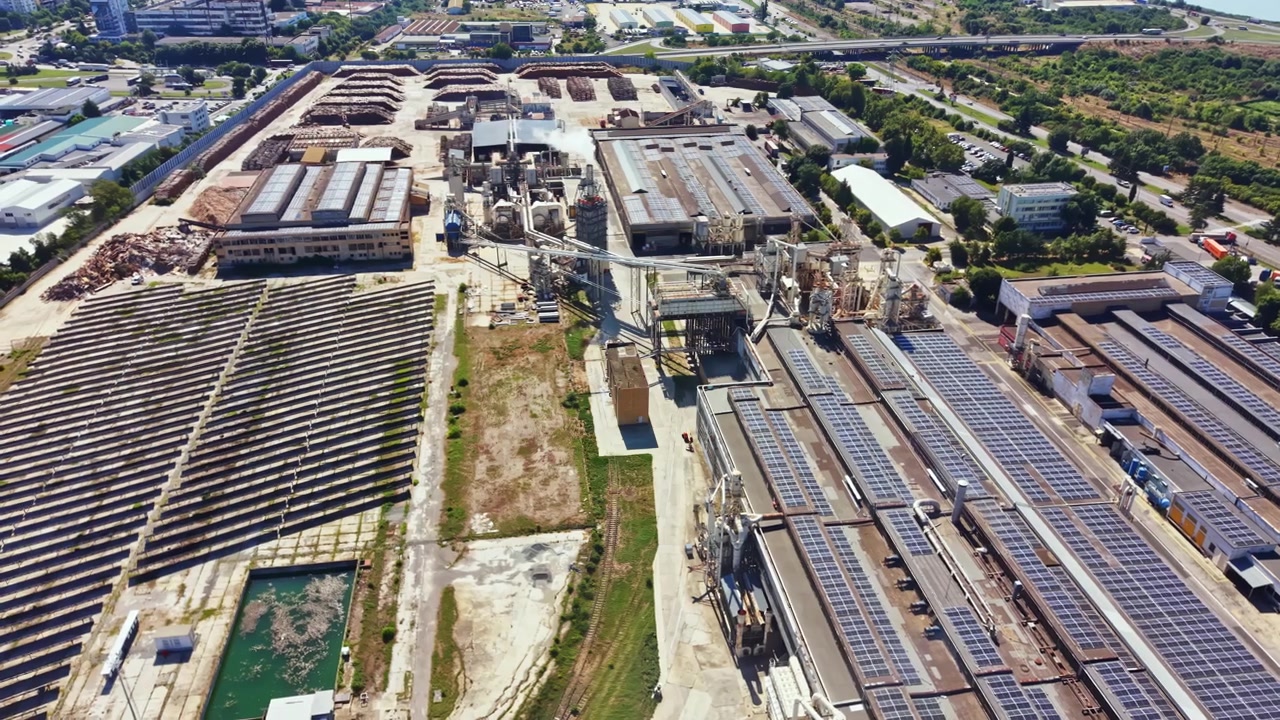 View of an industrial area with factories and solar panels next to a green landscape during daylight hours