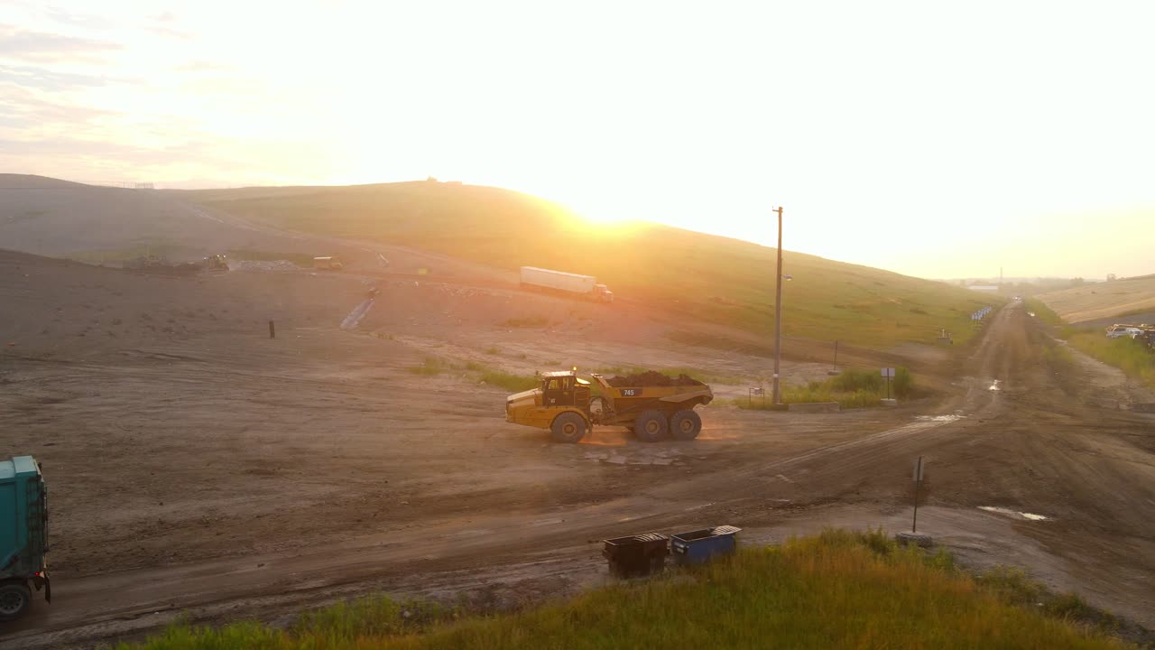 Semi truck and dump truck transporting material to landfill in Michigan during bright sunrise, aerial view