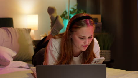 young woman relaxing in bed with laptop and phone