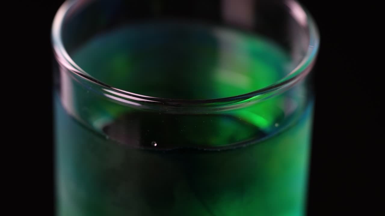 Close-up of green liquid swirling in glass, dark background, dramatic lighting, minimal camera movement