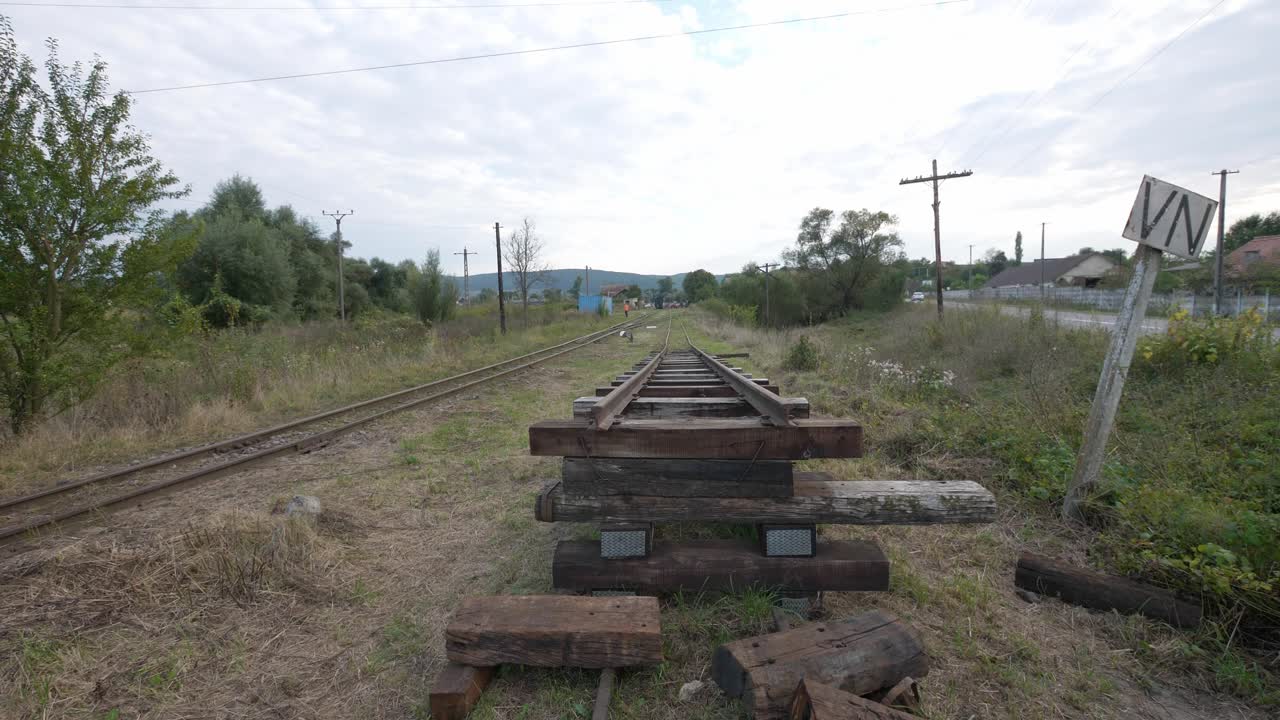 A smooth push-in shot moving forward along a rustic, single-track railway. The camera travels over the end buffer, creating a POV perspective of a journey into the countryside
