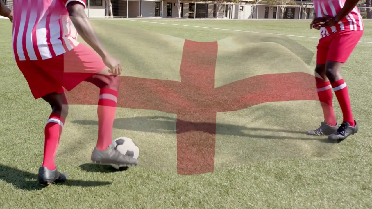 Dois jogadores de futebol treinando, o jogador da direita driblando a bola, com uma bandeira à esquerda cobrindo o centro.