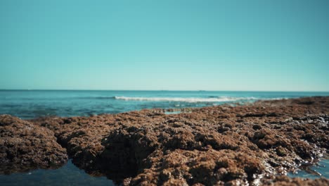 La-Costa-Del-Océano-Con-Barcos-De-Carga-Planos,-Las-Olas-Golpean-Las-Rocas-Suavemente-Fuera-De-Foco-Al-Sol-4k