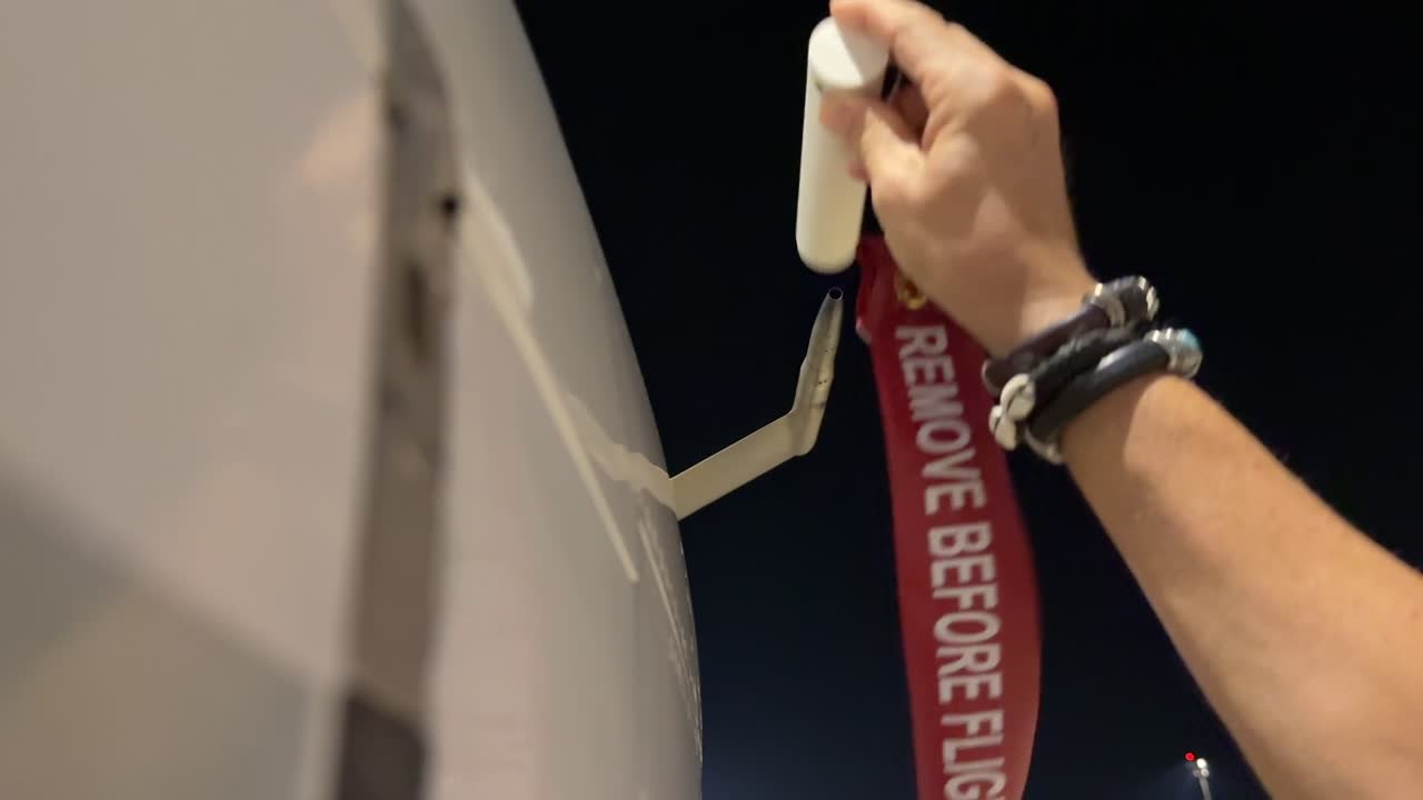 External view of the hand of a caucasian pilot removing gently the Remove Before Flight red tag before the first flight of the day at nifghttime