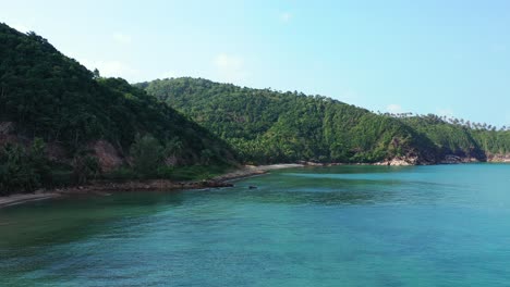 Beautiful-secluded-coast-of-tropical-island-with-rocky-slopes-going-down-to-seabed-under-calm-clear-water-of-blue-lagoon-in-Koh-Pha-Ngan,-Thailand