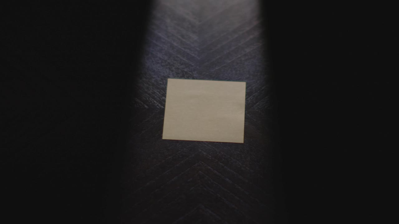 Slow motion close up footage of a hand writing out "I Love You" on a paper note and placing it on a table. Shot in dramatic lighting for an impressive title or transition