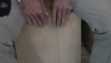 manos tocando un tambor de cajón de madera, mostrando movimientos rítmicos de las manos