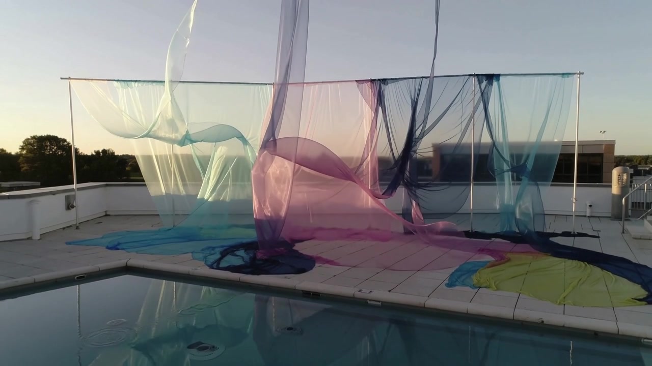 Brezza leggera che solleva pannelli tessili trasparenti, tendaggi che si muovono sopra una piscina sul tetto e un ponte piastrellato.