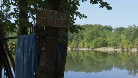 un cartel clavado en un árbol dice que no está permitido nadar en el lago de pesca búlgaro.