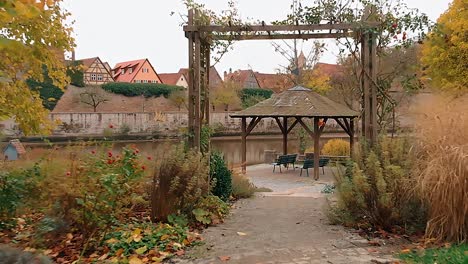 un dron vuela bajo y pasa lentamente a través de un arco de madera y luego a través de un cenador junto al estanque mientras continúa volando sobre el lago y en frente hay una ciudad histórica en alemania