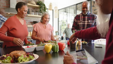 happy diverse senior female and male friends preparing food together in kitchen, slow motion