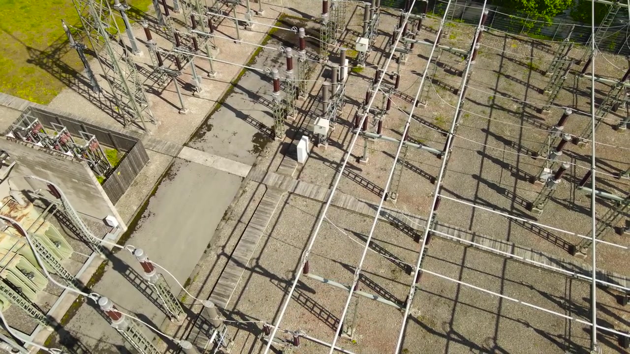 High voltage electrical power station with transformers and insulators for energy distribution and transmission, showing the infrastructure and network of cables from an aerial top down perspective