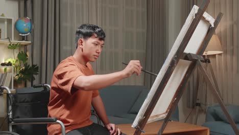 asian artist boy in wheelchair holding paintbrush mixed colour and painting on the canvas