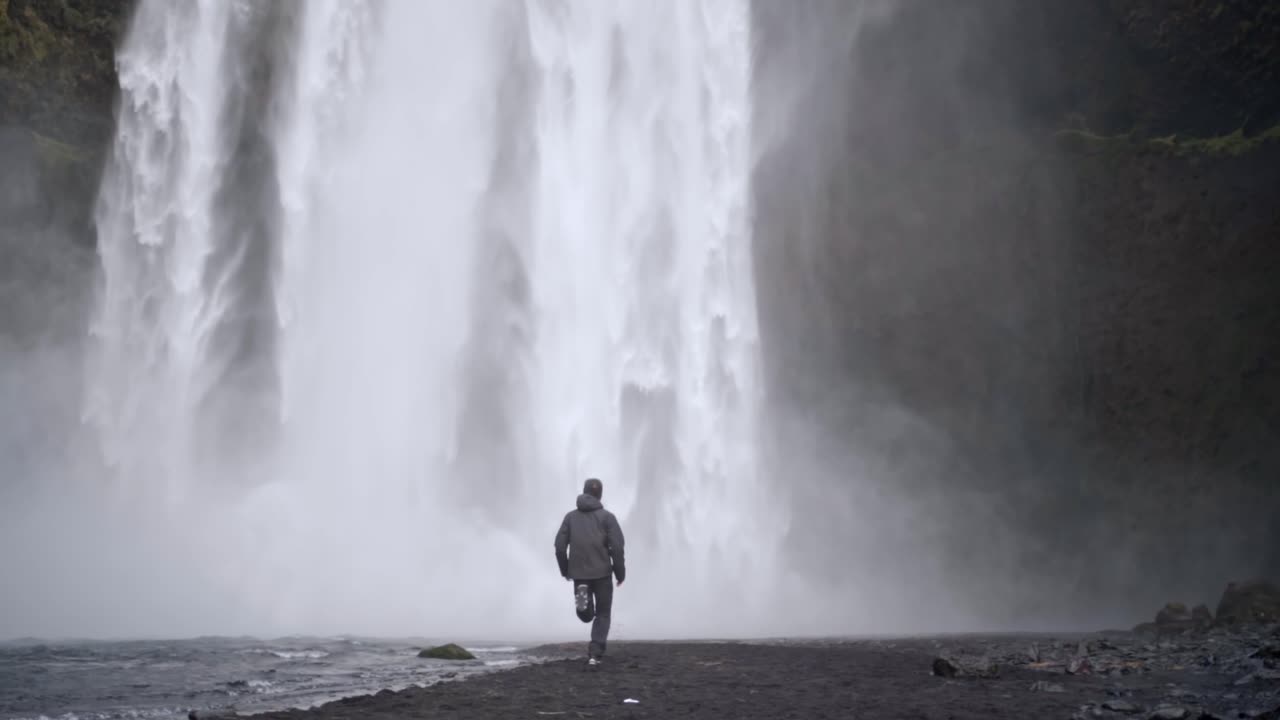 Man in outdoor gear running to the powerful mist of Skógafoss waterfall in Iceland