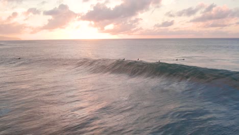 wave crashes in front of surfers at north shore, sunset aerial