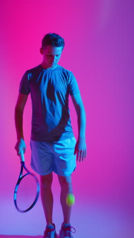 Vertical-Video-Studio-Shot-Of-Male-Tennis-Player-Bouncing-Ball-On-Racket-Against-Low-Key-Colourful-Mixed-Lighting-1