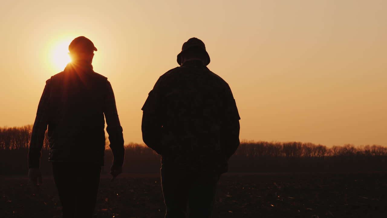 Vater und Sohn, beide Bauern, gehen bei Sonnenuntergang plaudernd über das Feld.
