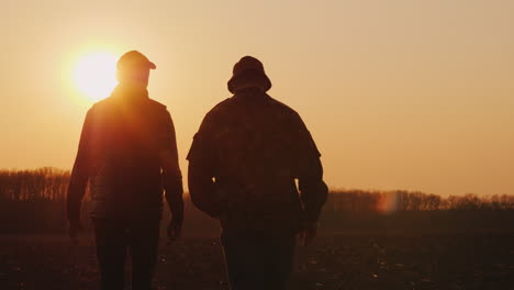 Farmers-Father-And-Son-Walk-Across-The-Field-At-Sunset-Chatting