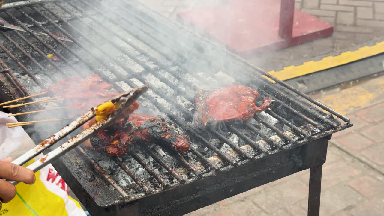 Close-up em câmera lenta de um vendedor grelhando carne marinada em uma churrasqueira a carvão que solta fumaça.