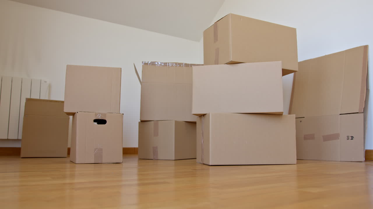Low POV static shot of woman picking up one of moving boxes and carrying it away