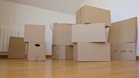 Low POV static shot of woman picking up one of moving boxes and carrying it away