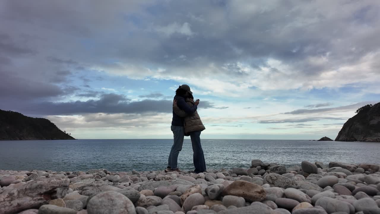 Couple embracing on rocky beach while facing the ocean