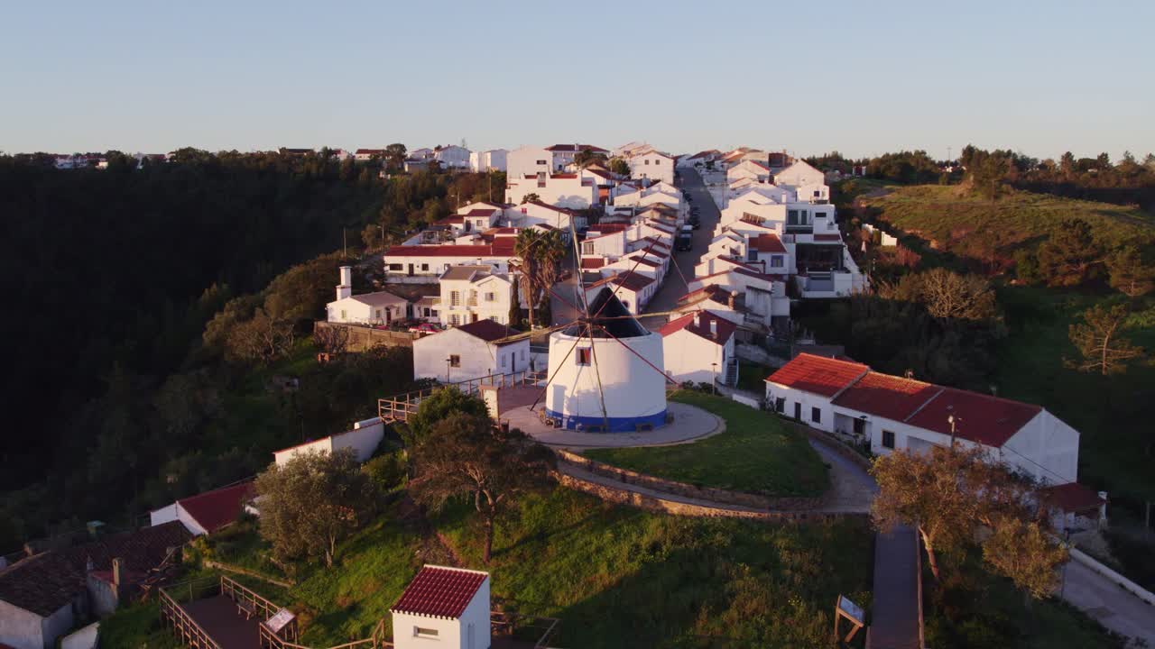 Vista aérea de Odeceixe com moinho de vento, aldeia tradicional, mostrando uma paisagem histórica dourada em Portugal