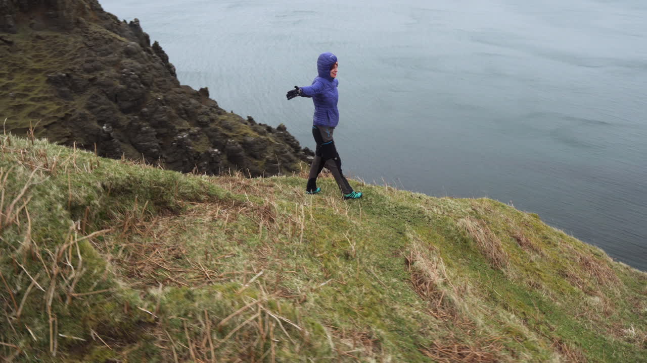 foto de seguimiento de una chica feliz disfrutando al borde de los acantilados en escocia, isla de skye con el océano atlántico al fondo en un día nublado