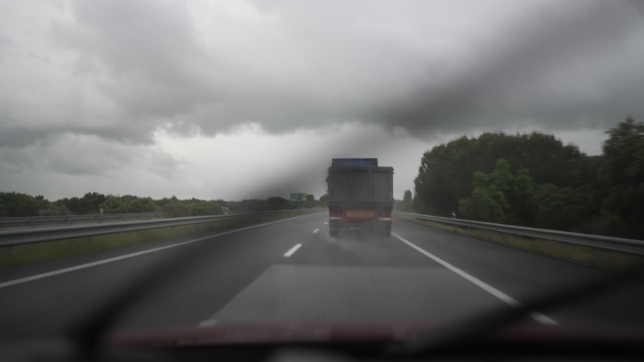 Truck driving on a highway under cloudy skies with rain and blurred road perspective